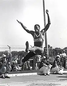 Photo de Carl Lewis lors d'une compétition de saut en longueur les bras levés avant de retomber dans le bac à sable