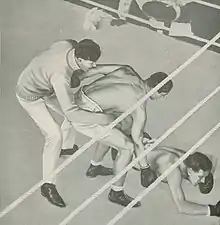 Retenu par l'arbitre, un boxeur tente de relever son adversaire, étendu au sol.