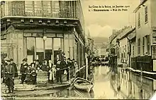 Personnes groupées à gauche devant un édifice et rue inondée à droite.