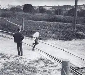 Un homme avec un béret passe sur un chemin de fer, un homme en costume le regarde.