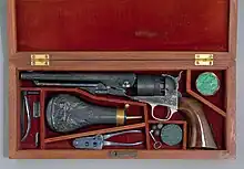 Photographie en couleurs d'un coffret contenant une arme à feu ancienne et ses accessoires.