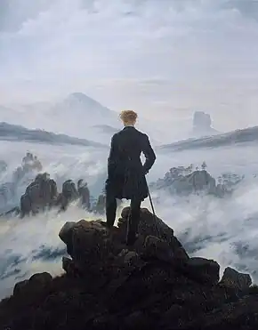  Tableau d'un homme debout tournant le dos au spectateur. Il est en haut d'une montagne, entouré de nugages et de brouillard. Il est vêtu de noir, en vif contraste avec les blancs, les roses et les bleus du ciel. Au lointain, on peut distinguer des affleurements de roches.