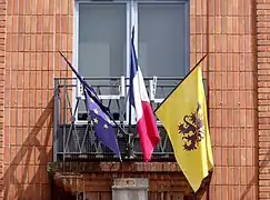 Drapeau de Flandre sur la façade de l'hôtel de ville de Cassel au côté des drapeaux français et européen.