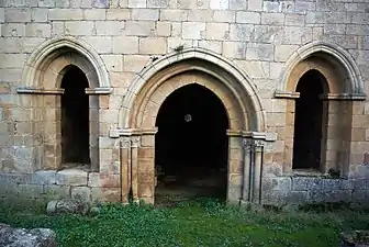 Mur de Pierre percé d'une porte en ogive flanquée de deux fenêtres également ogivales.