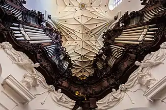 Photographie en contre-plongée d'un orgue en fer à cheval surmonté d'une voûte blanche à nervures décorée d'étoiles.