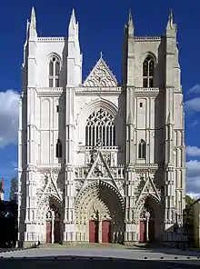 Façade : deux tours carrées encadrent la nef, bâtiment de style gothique en tuffeau blanc.