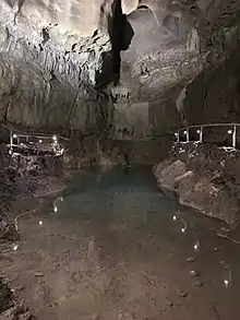 Photo en noir et blanc d'une grotte éclairée de part et d'autre. Au milieu, un cours d'eau.