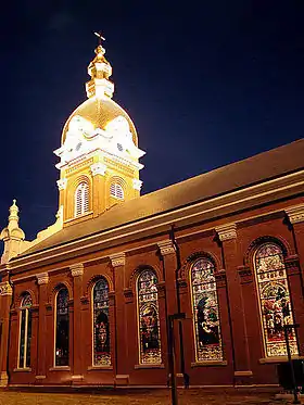 Photographie de nuit d’une église avec de hauts vitraux, et un clocher illuminé.