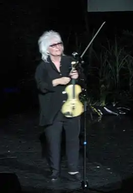 Femme en pied et de face, aux cheveux gris avec un violon.