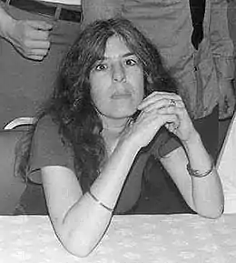 photographie en noir et blanc d'une femme assise derrière une table sur laquelle elle croise les mains