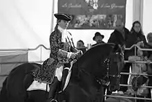 Photographie en noir et blanc représentant un Murgese de profil monté par une cavalière en costume baroque