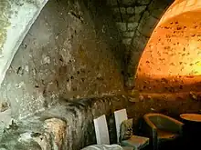 Photographie d'une cave où une banquette en pierre figure l'emplacement d'une ancienne tour.