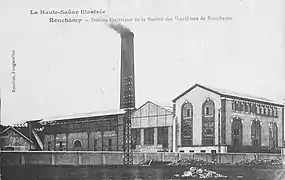 Autre vue de la centrale avec un grand bâtiment typés 1900 avec de grandes baies vitrés arrondies, à l'arrière la cheminée.