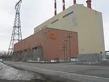Arrière de la centrale de Tracy, un bâtiment industriel avec 4 cheminées. À gauche, on voit un gros pylône électrique.