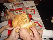 A number of hands break open a pale loaf made of several smaller buns