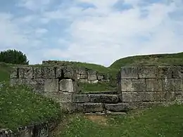 Une entrée en pierre, site en ruine et recouvert d'herbes.