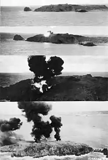 Quatre photos en noir et blanc montrant les étapes d'une explosion sur une île longiligne : d'abord l'île sans impact, puis une petite explosion sur la deuxième image, puis une grosse boule de feu entourée de fumée, et enfin, sur la quatrième image, apparaissent un grand incendie et une épaisse fumée noire.