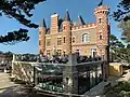 La façade ouest du château du Nessay avec sa terrasse au-dessus du restaurant qui abrite une belle collection de dame-jeanne derrière la vitre.