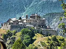 Un château-fort entouré de remparts de style Vauban, sur une butte dans une vallée de montagne.