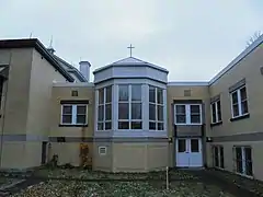 Un oriel surmonté d'une croix saillant d'un bâtiment revêtu de brique beige.