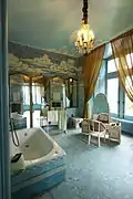 Photographie en couleurs d'une pièce équipée de baignoire, lavabo et dont les murs sont décorés de mosaïque à dominante bleue.