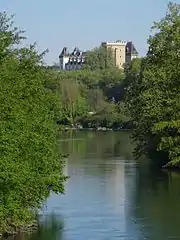 Photographie en couleurs d'un cours d'eau aux rives boisées ; château en surplomb en arrière-plan.