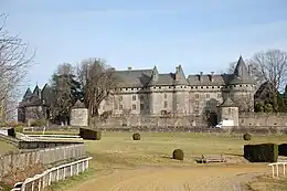 Photo d'un château gris avec des tourelles dont le parc s'étandant à ses pieds rejoint la piste d'un hippodrome.