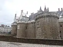 Photographie en couleurs des remparts et des tours d'un château en pleine ville.