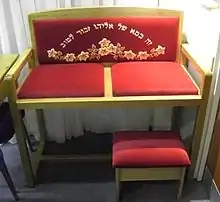 Photographie couleur d'une chaise portant des coussins rouge et une inscription en lettres hébraïques.