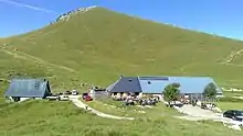 Deux bâtiments aux toits en taule bleutée sous un sommet couvert d'alpages.