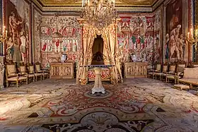 Photo couleur présentant une pièce avec lit à baldaquin et de riches tapisseries aux murs.