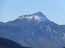 Montagne enneigée dominant une barre rocheuse en avant-plan.