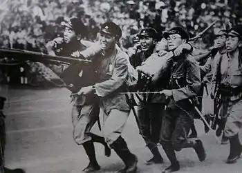 Photo noir et blanc de quatre hommes, les traits tirés par l'effort, en tenue militaire et armés, portant un cinquième homme.