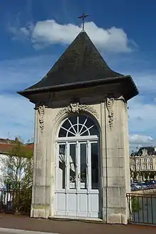 Petit édifice en pierre avec une porte vitrée, surmonté d'une croix.