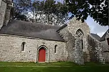 À gauche, porte encadrée de minuscules fenêtres très étroites. À droite, le croisillon avec sa grande fenêtre et ses deux gigantesques contreforts.