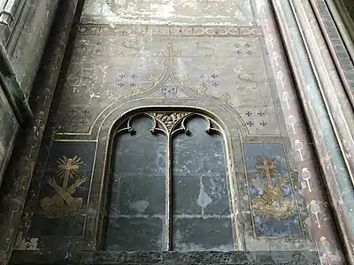 Mur de pierre peint. En haut, les lettres F et S sont entrelacées. En bas, de part et d'autre d'une niche vide, sont peints deux bras croisés devant une croix.