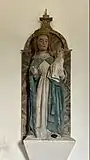 photo en couleurs de la statue de la Vierge à l'Enfant sur un socle blanc fixé au mur.