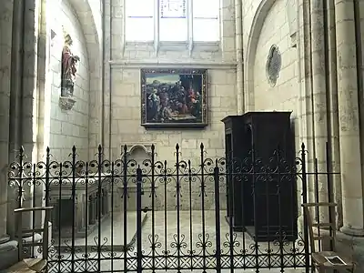 Pièce fermée par une grille en fer forgée, contenant un tableau, une statue et un confessionnal.