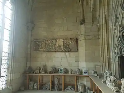 Pièce avec des murs de pierre dans laquelle sont disposées des dizaines de morceaux de sculptures. Accroché au mur, un bas-relief très dégradé