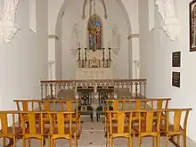 Intérieur de la chapelle, bancs d'église, prie-dieu, vitraux autel et chandeliers liturgiques.