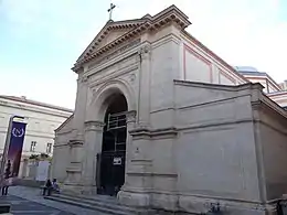 Photo en couleurs de la façade néoclassique de l'entrée de la chapelle surmontée d'un fronton corinthien, de couleur rose pâle
