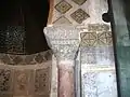Vue d'un chapiteau du mihrab. En forme de tronc de cône renversé, il est coiffé d'un abaque richement sculpté, lequel est surmonté d'un mince bandeau épigraphique en caractères coufiques.