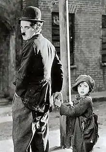 Photographie de Charlot l'air énervé tenant la main à un petit garçon en haillons