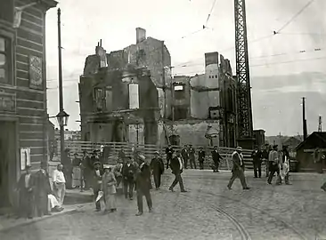 Photo ancienne en noir et blanc d'un bâtiment ruiné dans une rue où passent des gens.