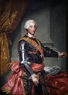 Charles III de trois-quart, un manteau posé sur une table. La main droite tient un bâton, la gauche pointe du doigt.