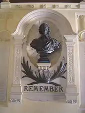 Buste noir devant un relief mural portant l'inscription « Remember ».