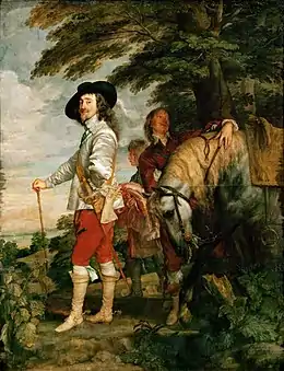 Charles Ier portant une veste grise, un pantalon rouge, des bottes, une canne et un chapeau noir et une tenue d'équitation se tient sous un arbre aux côtés d'un cheval et de son écuyer.