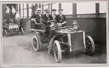 Une voiture du début du siècle occupée par quatre hommes portant des chapeaux.