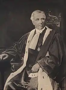 Photo en noir et blanc de Charles Jac en tenue de magistrat, assis sur un fauteuil.