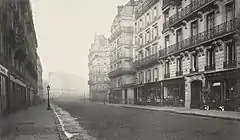 Photo en noir et blanc d'une large rue bordée d'immeubles haussmanniens.